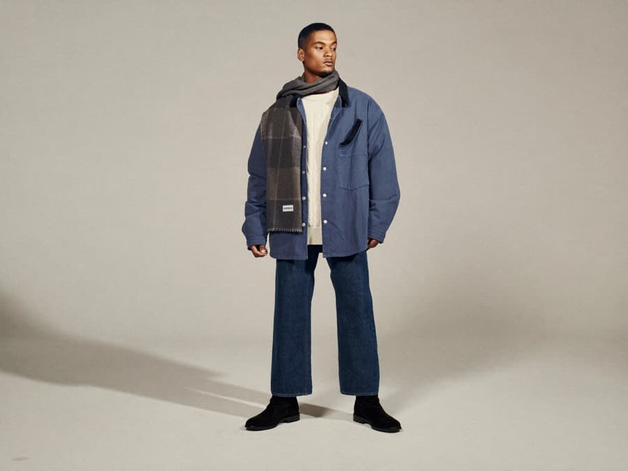 A model in a winter look layering a cream knit under a slate quilted overshirt with indigo denim